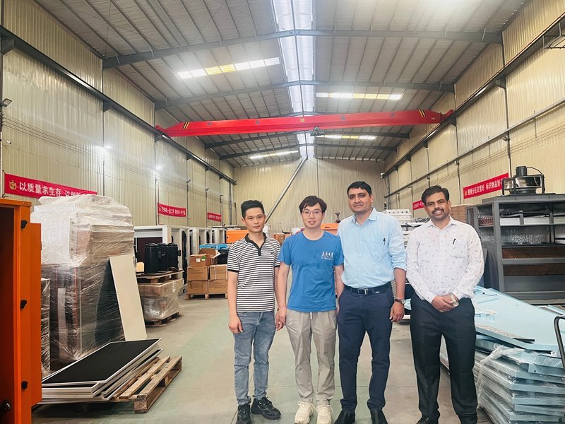Four visitors posing on the factory floor beneath the overhead crane