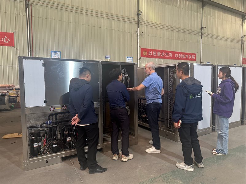 Visitors inspecting the open compressor compartment of a heat pump drying unit