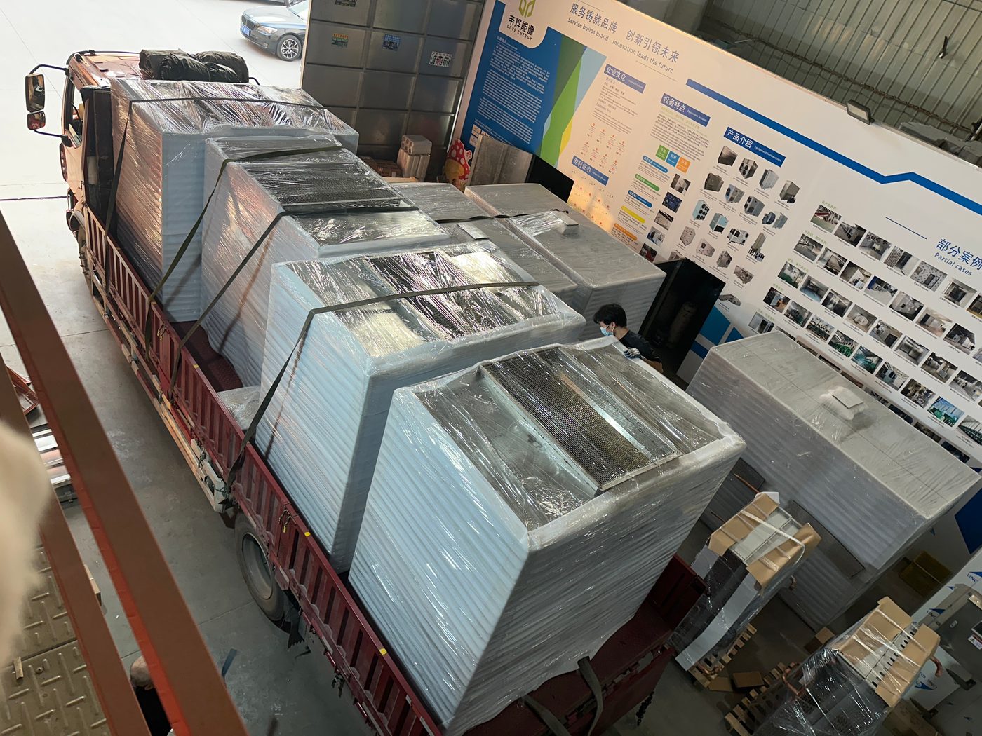 Shrink-wrapped heat pump units on a flatbed in front of the Diye brand wall
