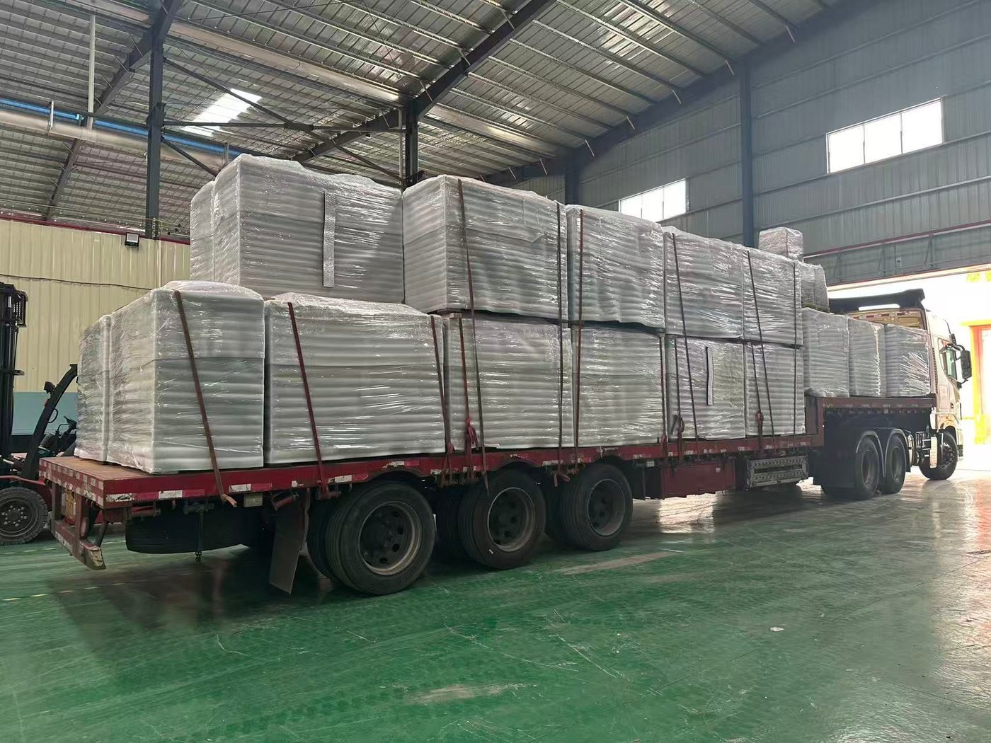 Two-high shrink-wrapped load secured with red straps, forklift alongside